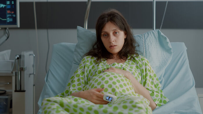 Young woman in hospital bed wearing a green polka dot gown, connected to medical devices, evoking scary ghost stories hospital work.