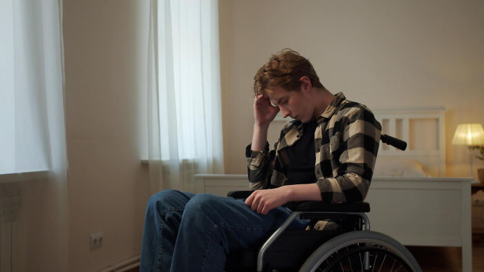Young man in a wheelchair looking distressed in a quiet room, highlighting challenges faced by people with disabilities.