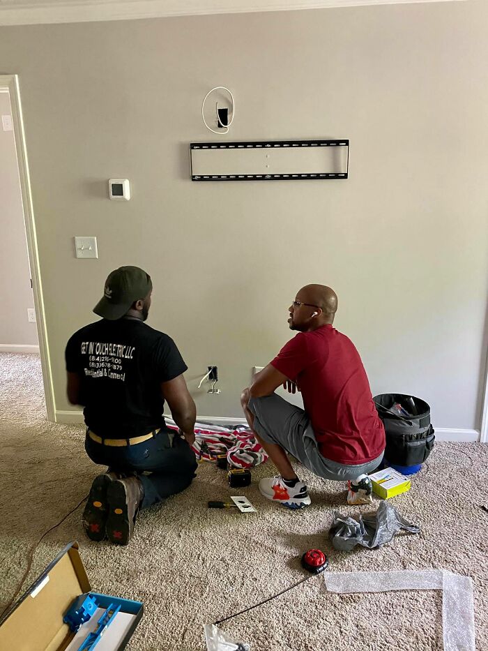 Two men kneeling on the floor fixing a wall outlet, showcasing faith in humanity restored through acts of kindness.