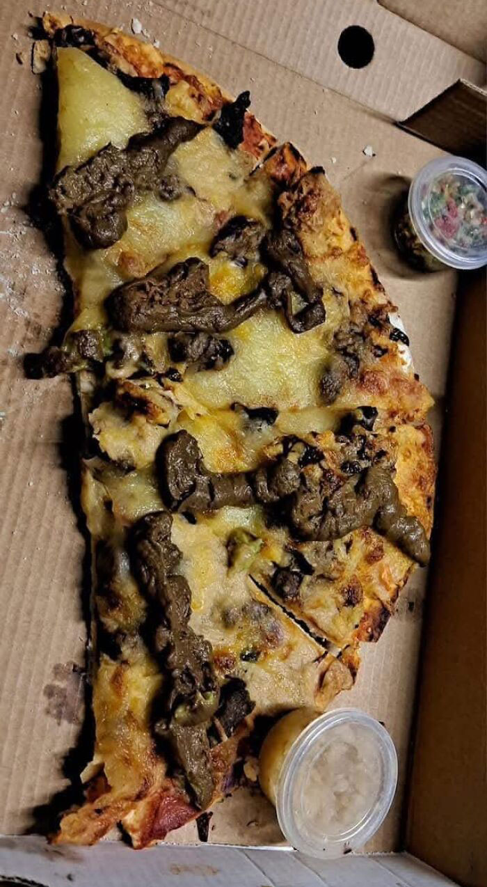 Pizza slice with melted cheese and dark, unappetizing toppings in a box, showing cursed and disgusting food appearance.