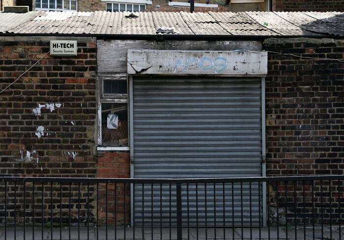 Old brick building with a closed metal shutter, graffiti, and a Hi-Tech security sign creating a creepy photo moment.