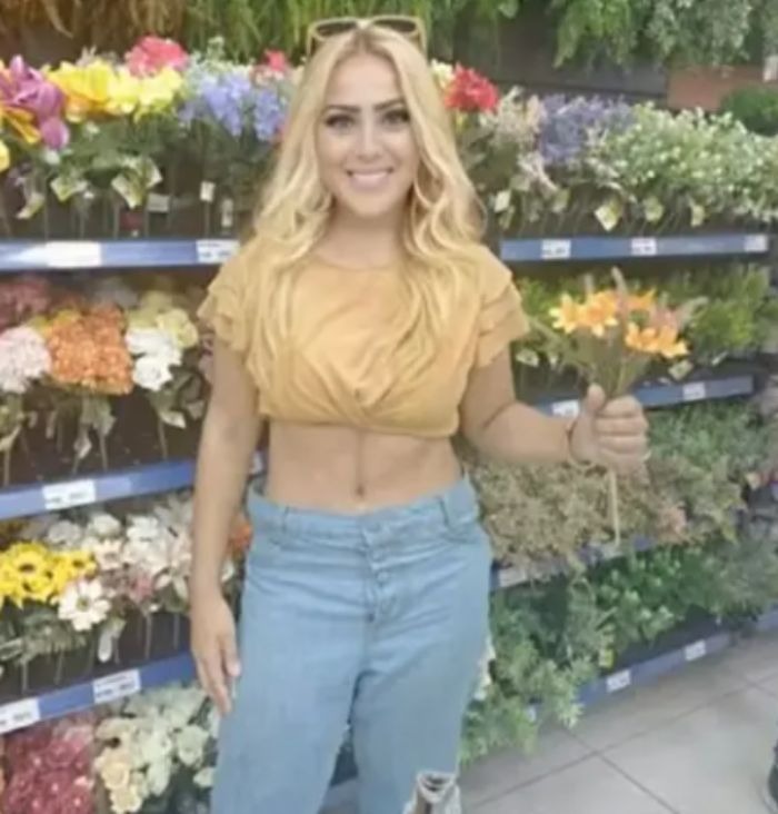 Young woman with an angel-faced appearance standing in front of flower displays holding orange flowers.