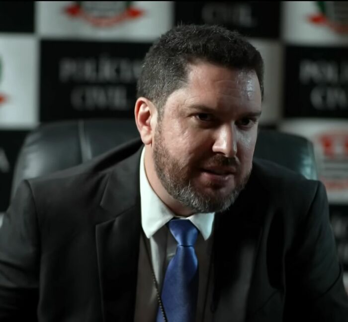 Man in a suit and blue tie giving a chilling confession about an angel-faced serial criminal in a dimly lit office setting.