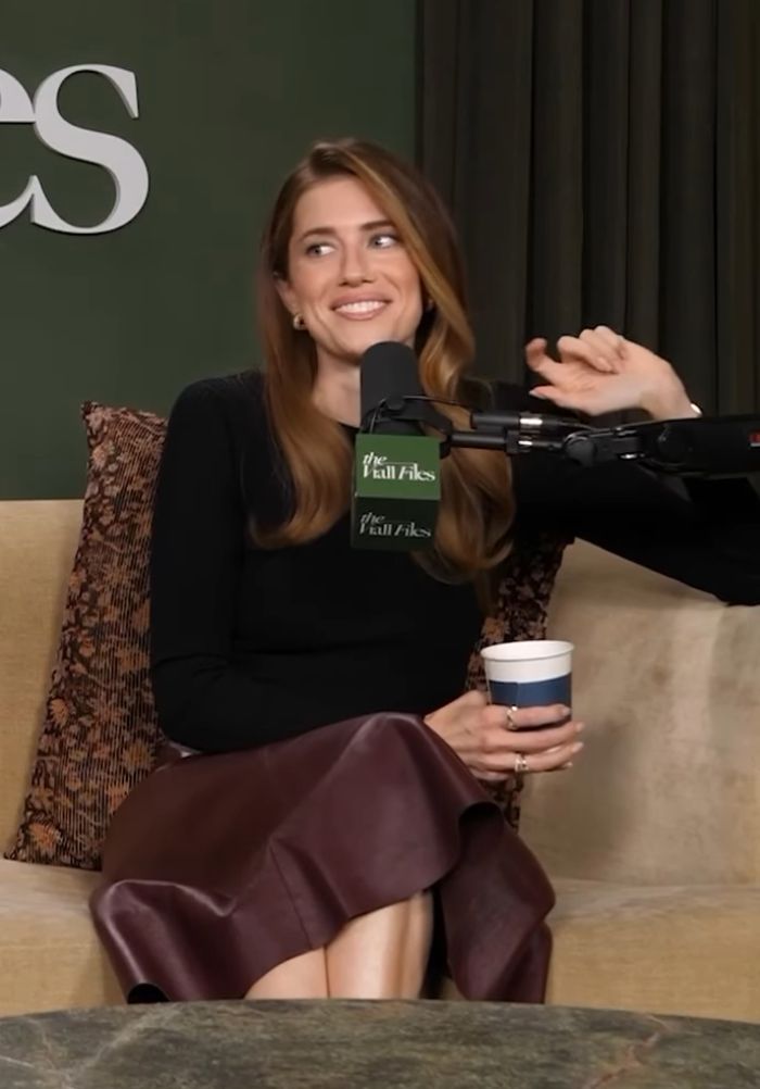 Allison Williams speaking on a podcast, smiling and holding a cup while discussing nepo babies and privilege.