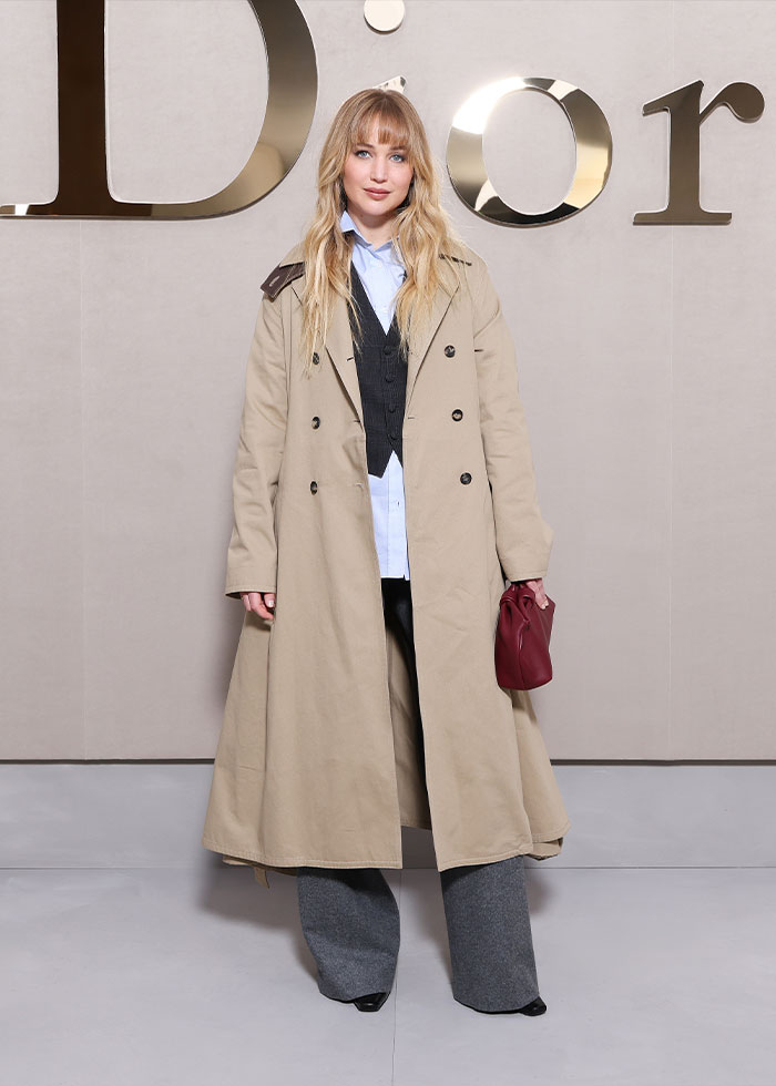 Woman in beige trench coat and gray pants posing at Paris Fashion Week 2025 celebrity looks event.