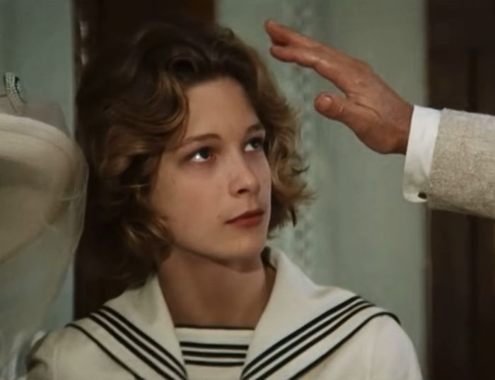 Young actor known as the most beautiful boy in the world in a vintage film scene with a raised hand nearby.