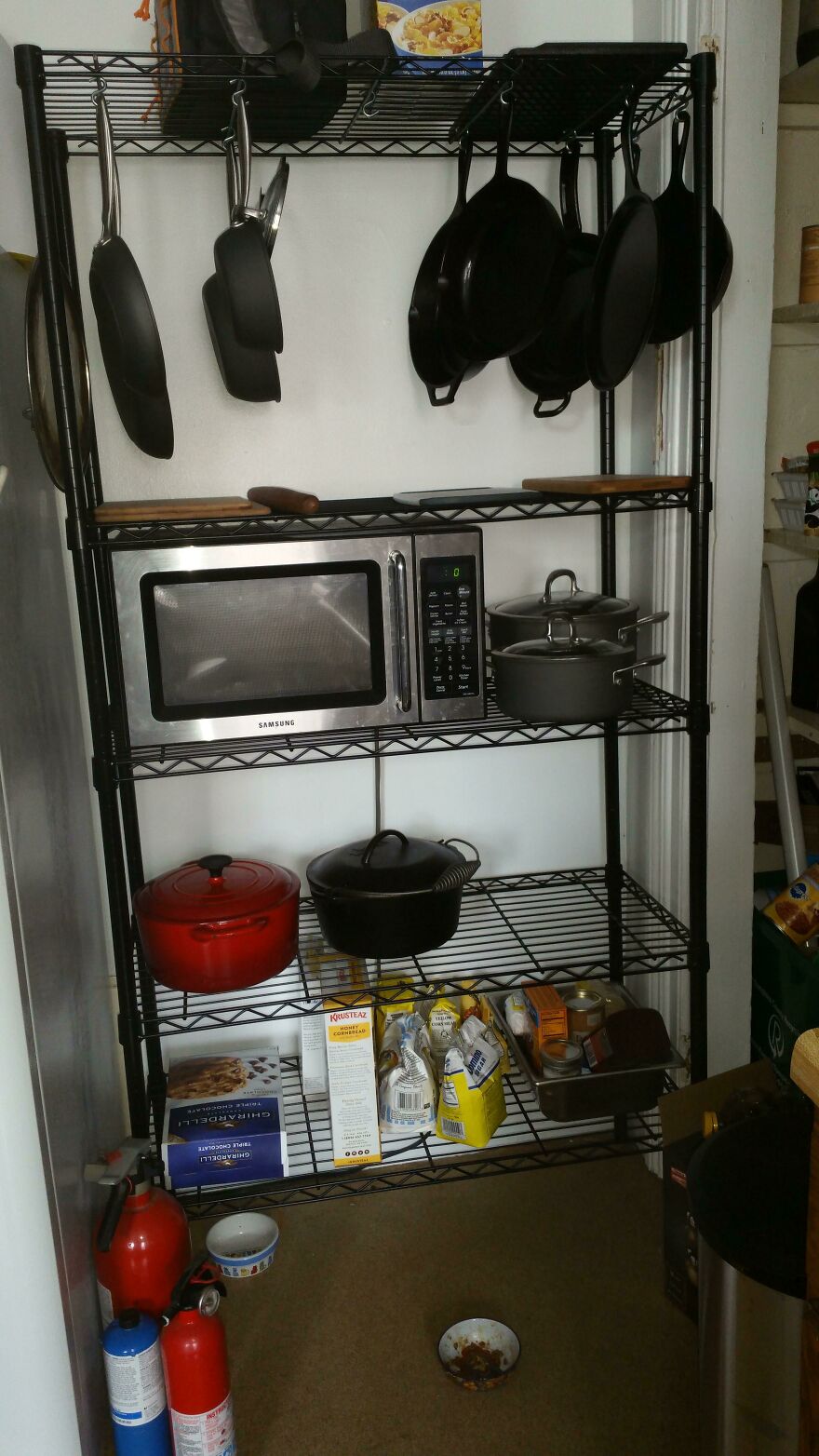 Metal kitchen shelf with pots, pans, microwave, and food items demonstrating organization hacks for home storage.