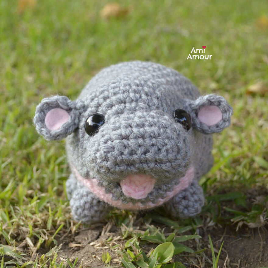 Crochet animal hippo with big eyes and pink details sitting on grass, showcasing charming personality and craftsmanship.