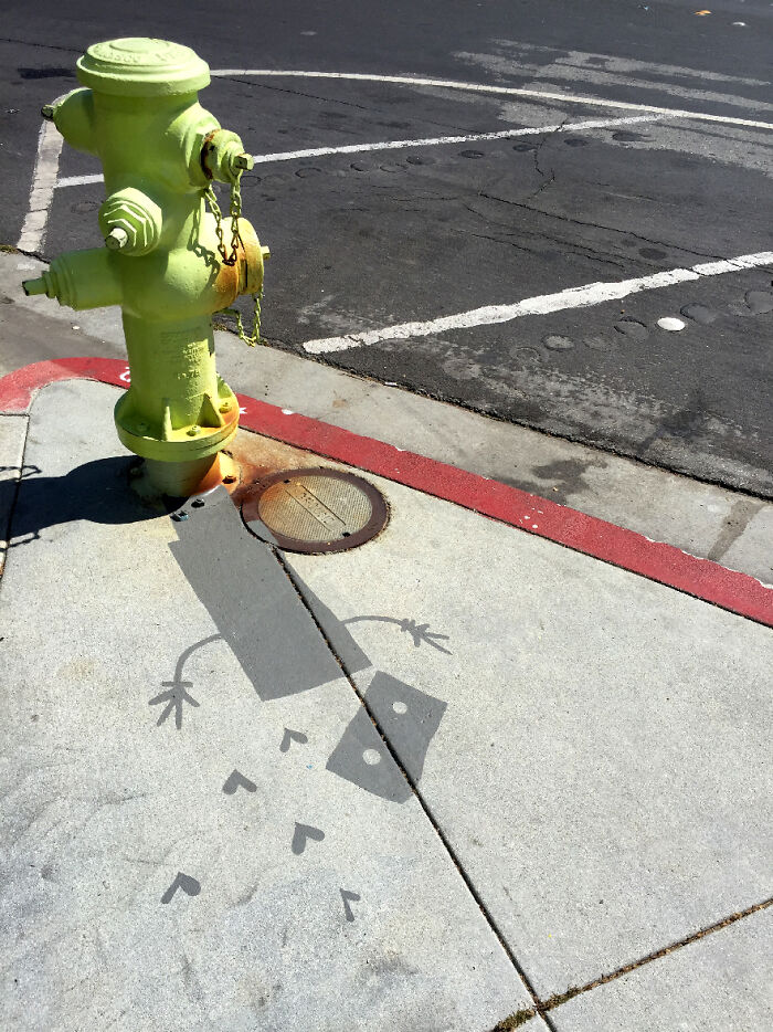 Green fire hydrant casting a clever shadow art installation of a robot figure on the sidewalk.