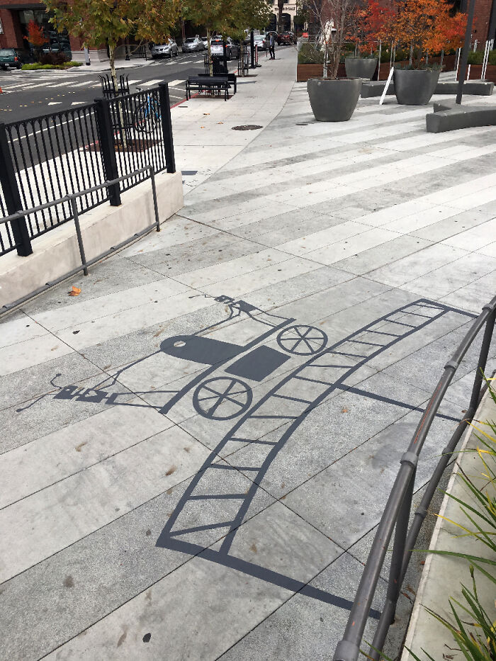 Shadow art installation on sidewalk creating an illusion of a vintage car on train tracks in an urban setting.