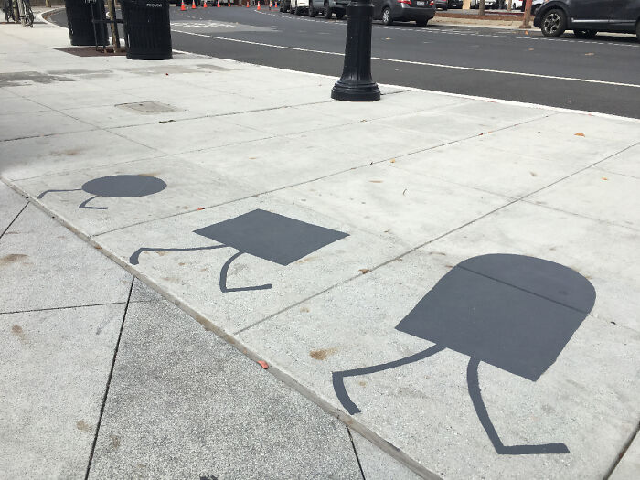 Shadow art installations on city sidewalk depict walking geometric shapes in urban environment.
