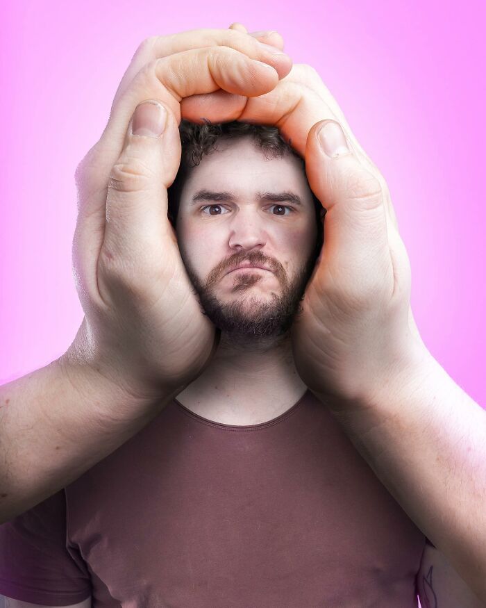 Man's face framed by giant hands in a surreal and logic-challenging photo manipulation with a pink background.
