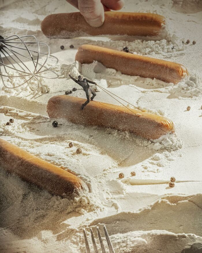 Logic-challenging photo manipulation of a miniature skier skiing over hot dogs on a flour-covered surface.