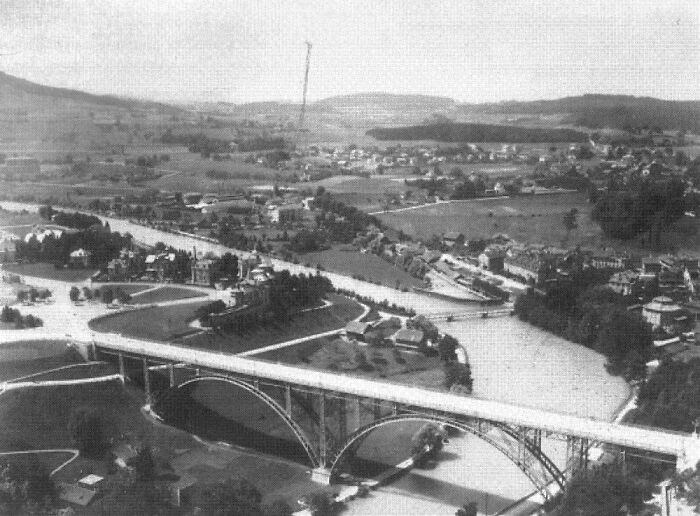 A black and white photo showing a historic view of a city with a large arched bridge over a river before modern times.