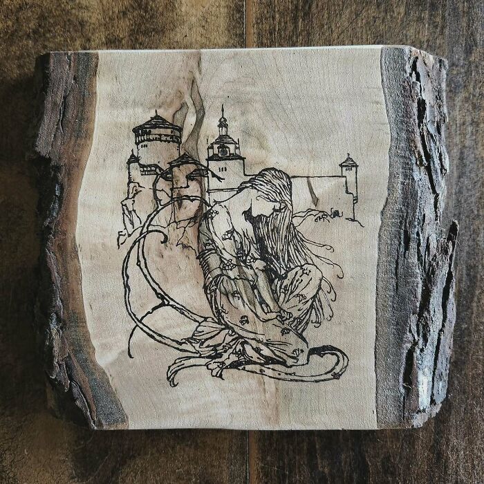 Wood-burned artwork by Canadian artist Kat Slota depicting a detailed figure and castle scene on a natural wood slab.
