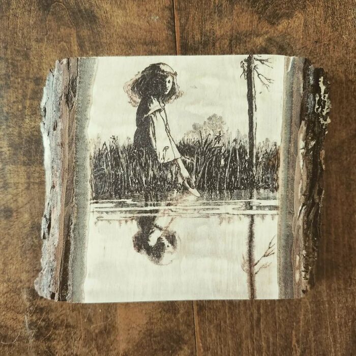 Wood-burned artwork by Canadian artist Kat Slota depicting a girl touching water, created using fire on wood.