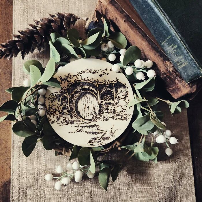 Wood-burned artwork by Canadian artist Kat Slota featuring detailed circular design surrounded by greenery and books.