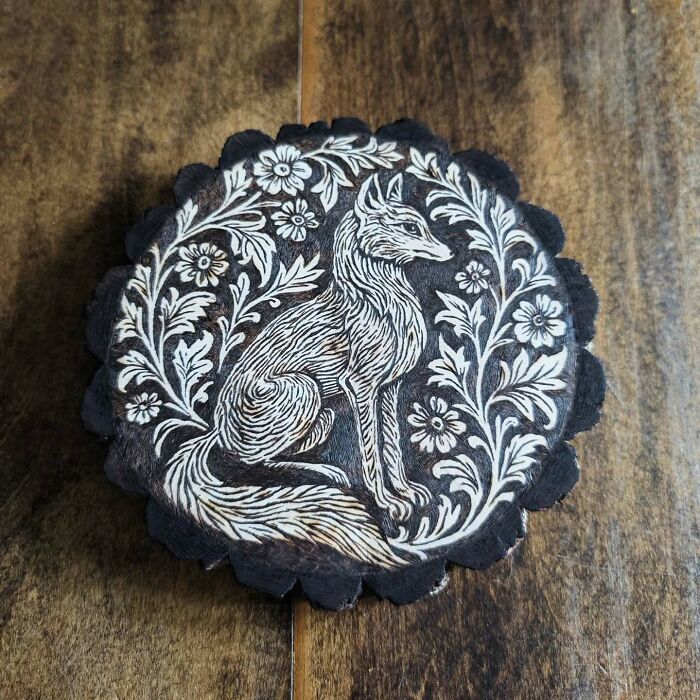 Wood-burned artwork of a detailed fox surrounded by floral patterns created by Canadian artist Kat Slota using fire.