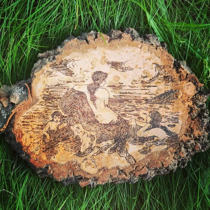 Wood-burned artwork by Canadian artist Kat Slota depicting mermaids on a natural wood slice using fire techniques.