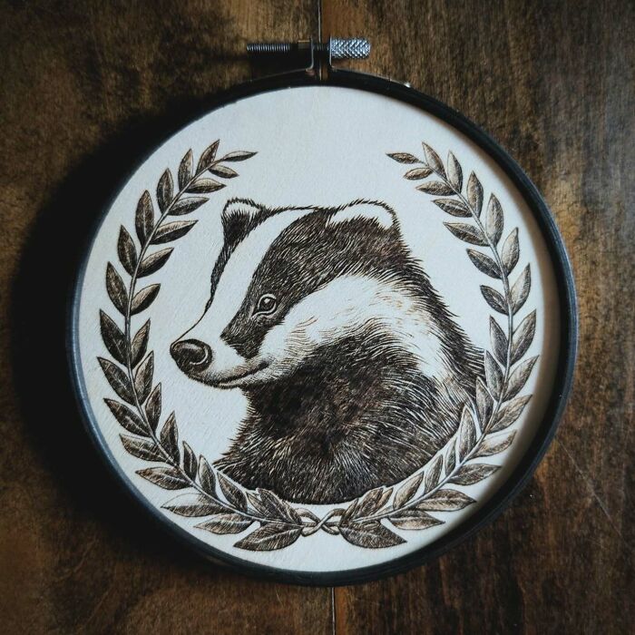 Wood-burned artwork of a badger framed with leaves, created by Canadian artist Kat Slota using fire for stunning effects.