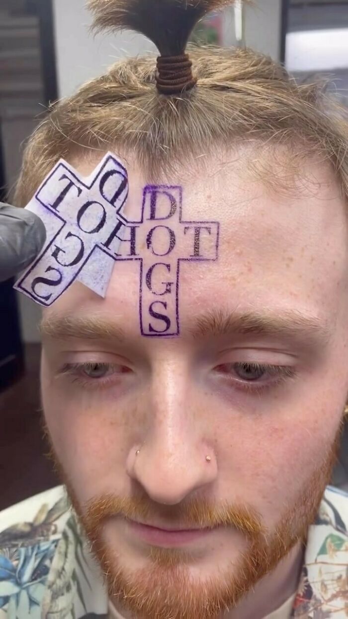 Close-up of a man getting an awful tattoo stencil of a cross on his forehead, highlighting poor tattoo decisions.