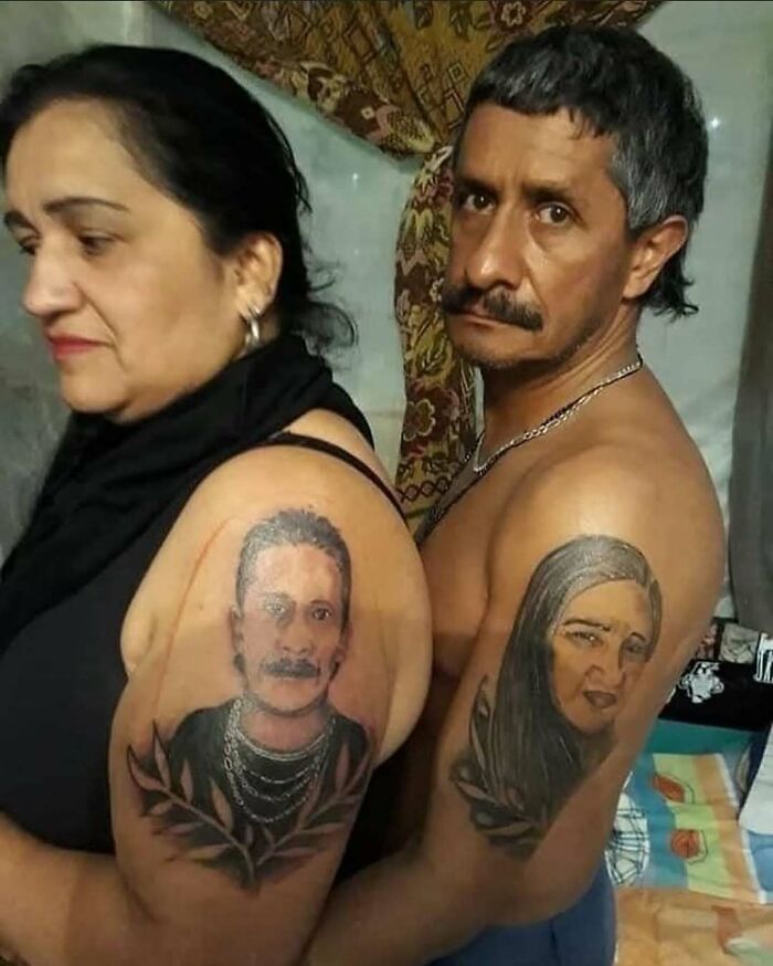 A man and woman showing awful tattoos of each other's portraits on their upper arms, showcasing poor tattoo decisions.