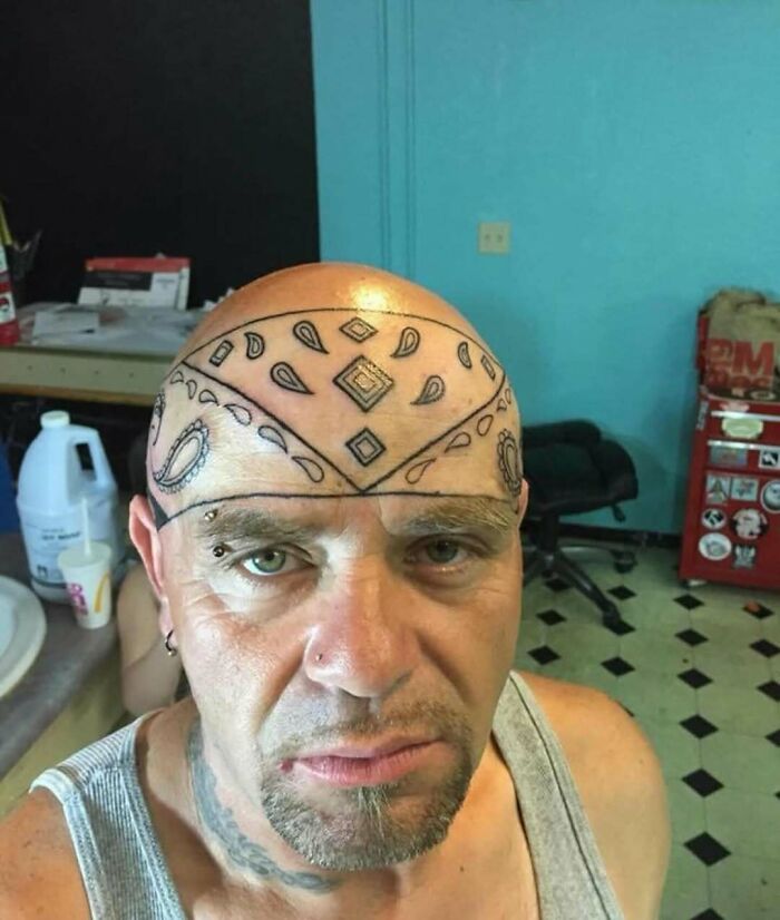 Man with an awful tattoo of a bandana design inked across his bald head, illustrating some of the worst tattoo decisions.
