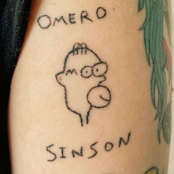 Tattoo of a poorly drawn cartoon character labeled Omero Sinson, an example of awful tattoos and bad decisions.