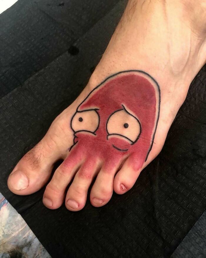 Foot tattoo of a cartoonish red squid with worried eyes, an example of awful tattoos and questionable smart decisions.