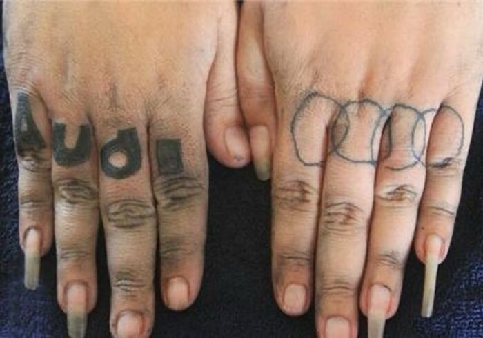 Close-up of two hands showing awful tattoos on fingers, highlighting poor tattoo decisions and questionable ink choices.