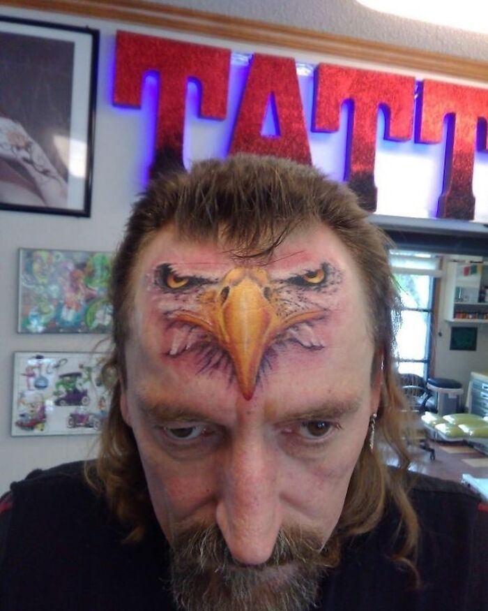 Man with an eagle face tattoo on his forehead, showcasing one of the most awful tattoos from the collection.