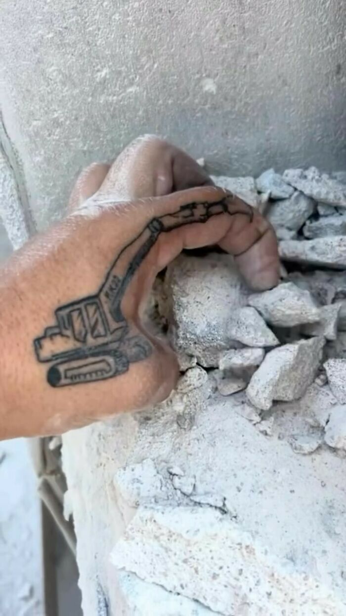 Hand with a tattoo of a construction excavator positioned over broken concrete, part of awful tattoos collection.
