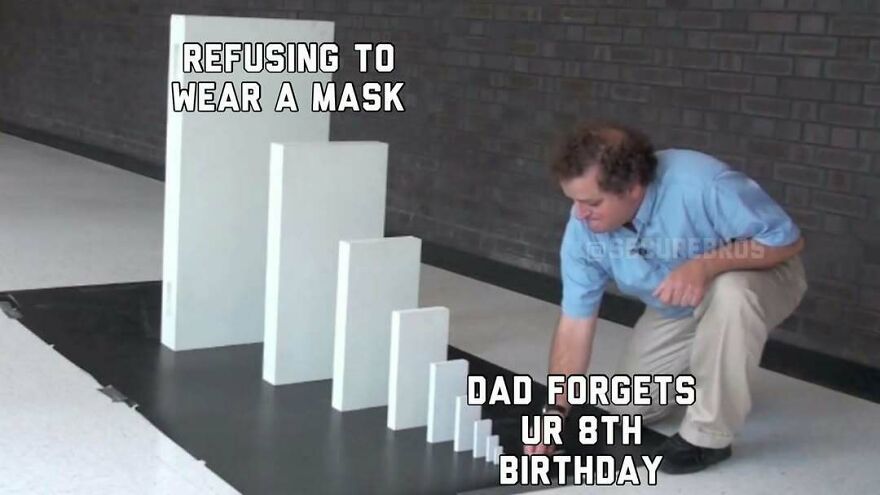 Man kneeling to push a small domino labeled dad forgets birthday, next to larger domino labeled refusing to wear mask, alpha males humor.