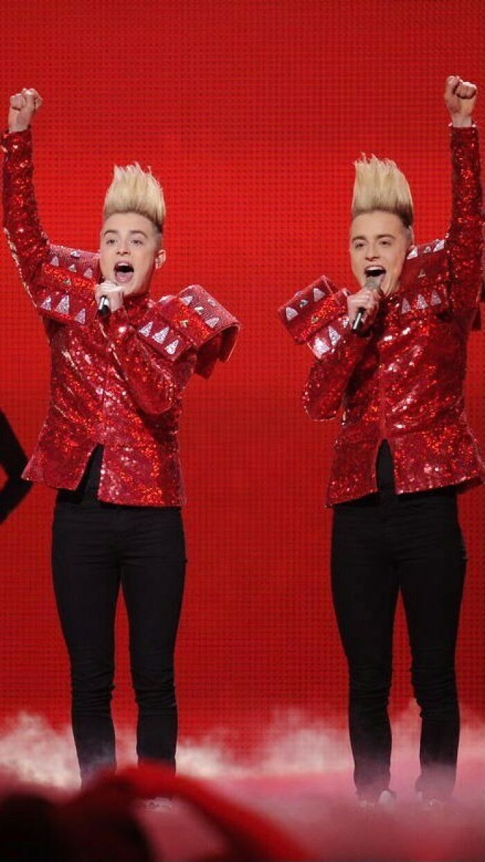 Celebrity twins performing on stage in matching red sequined jackets and black pants, showcasing unique hairstyles and energy.