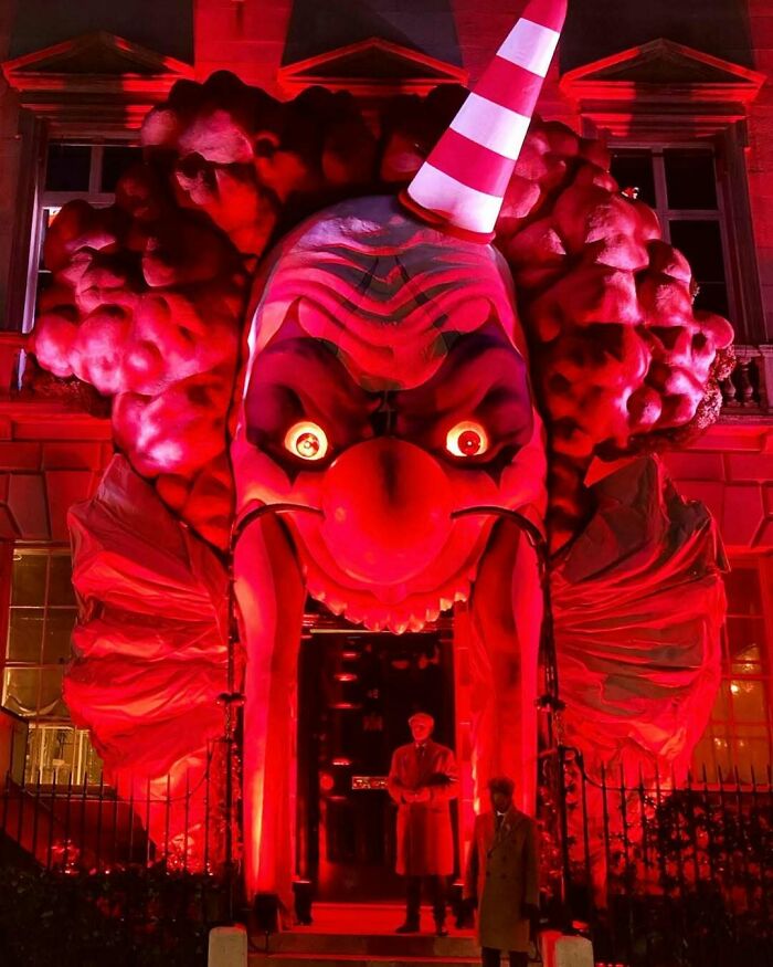 Giant scary clown outdoor Halloween decoration glowing red at night with people standing in front of the entrance.