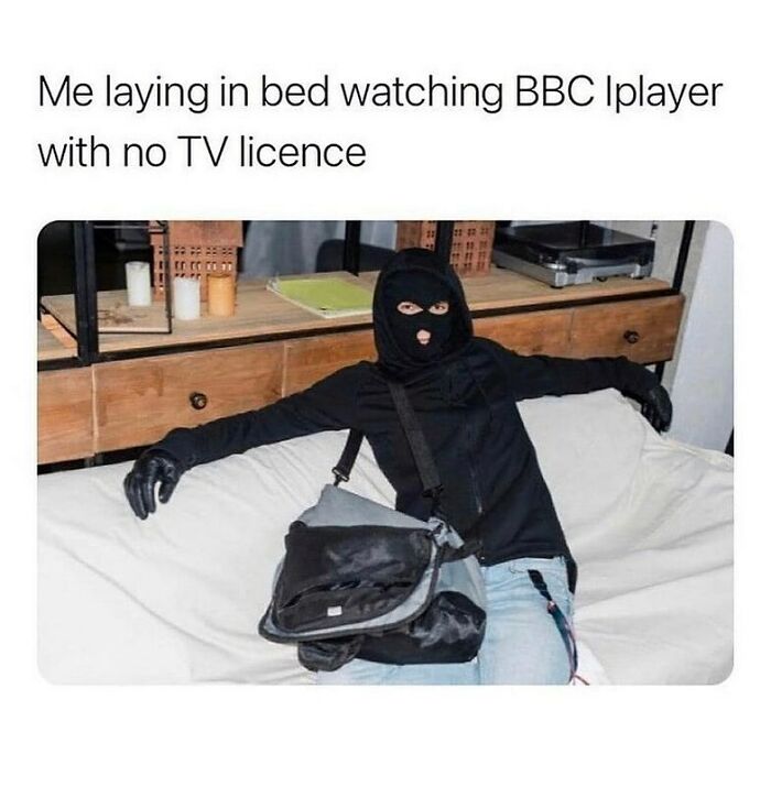 Person in black balaclava and gloves lounging on a couch, humorously referencing unapologetically British memes and posts.