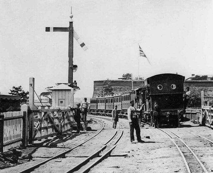 Historic black and white photo of a train station with workers beside railway tracks in old world capitals.