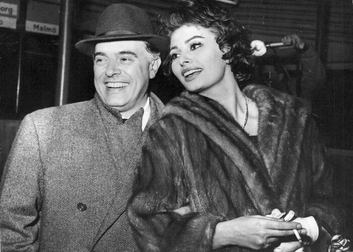 Sophia Loren smiling in a fur coat with a man in a hat, capturing Italian beauty and Hollywood legend charm.