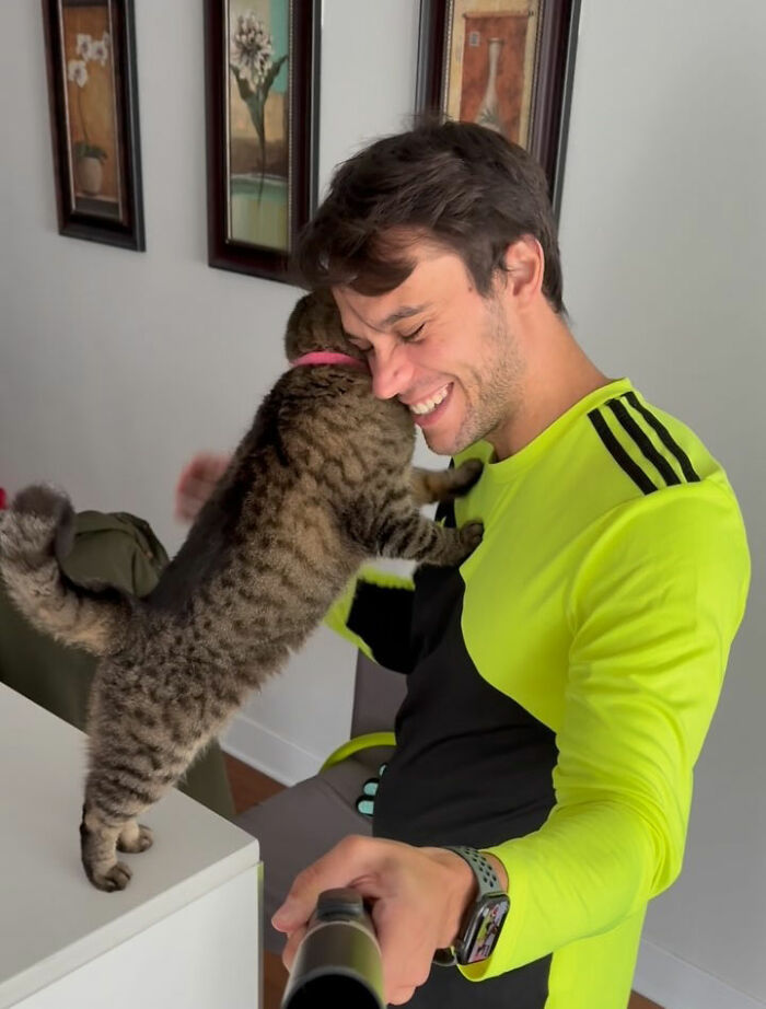 Man smiling as a cat climbs onto him, showing the cat's refusal to give up on finding love after being returned twice