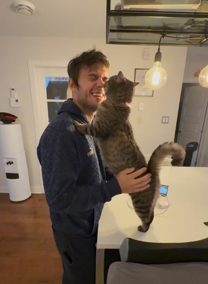 A man smiling while holding a tabby cat showing love, illustrating a cat refusing to give up on finding love.