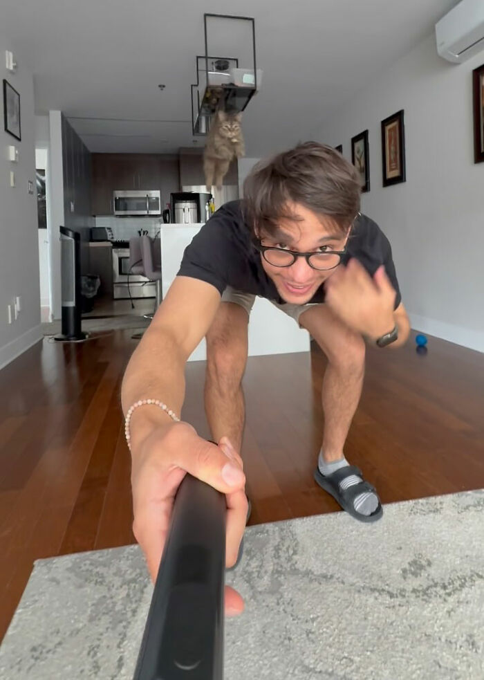 Man taking a selfie with a cat jumping in the background, showing the bond of a cat refused to give up on finding love.