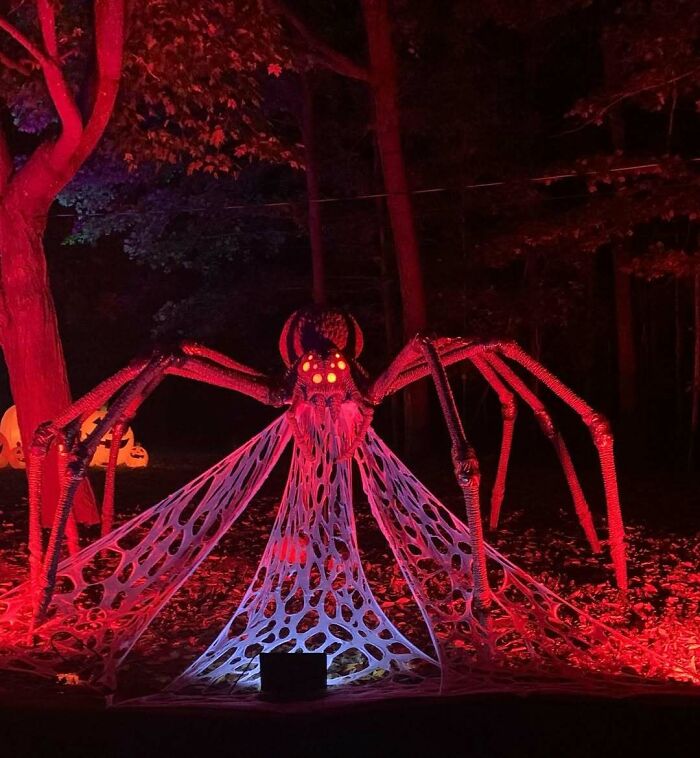 Giant spider Halloween outdoor decoration with glowing eyes and web, illuminated in red light at night.