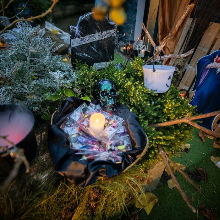 Outdoor Halloween decorations featuring a glowing skull, candle, candy baskets, and spooky tombstone in a garden display.