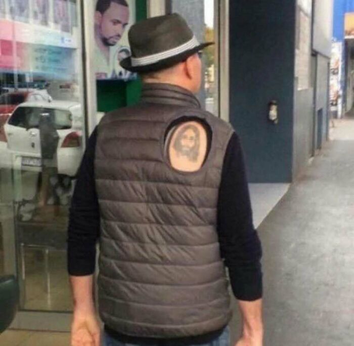 Man wearing a vest with a tattoo partially visible through a hole on the back, showcasing awful tattoos and poor decisions.