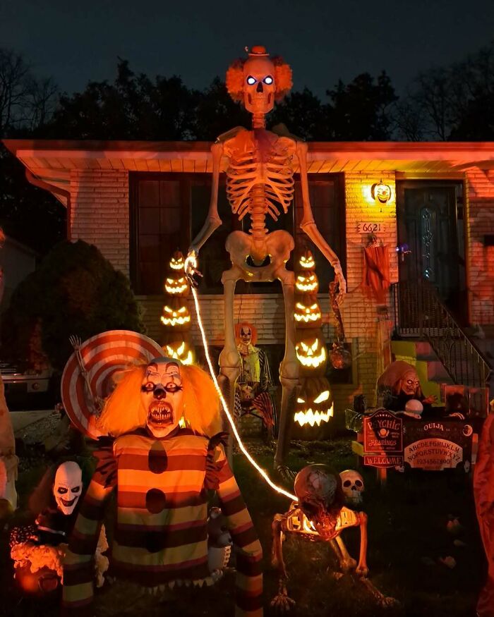 Outdoor Halloween decorations featuring glowing skeletons, creepy clowns, and illuminated jack-o'-lanterns at night.