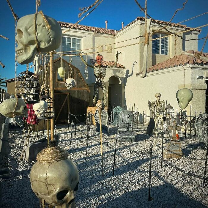 Outdoor Halloween decorations feature skulls, skeletons, tombstones, and spooky props in a front yard display.
