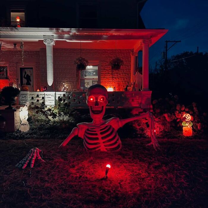 Large skeleton with glowing red eyes emerging from ground in a yard as part of outdoor Halloween decorations at night.