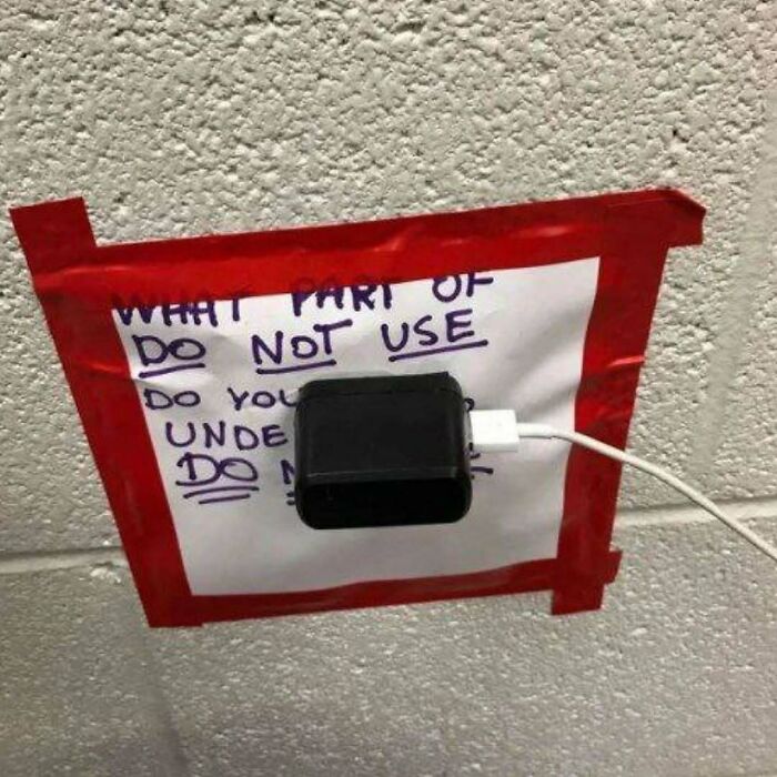 Charger plugged into a power outlet covered with a taped warning sign, fitting images that might need a priest or exorcist.