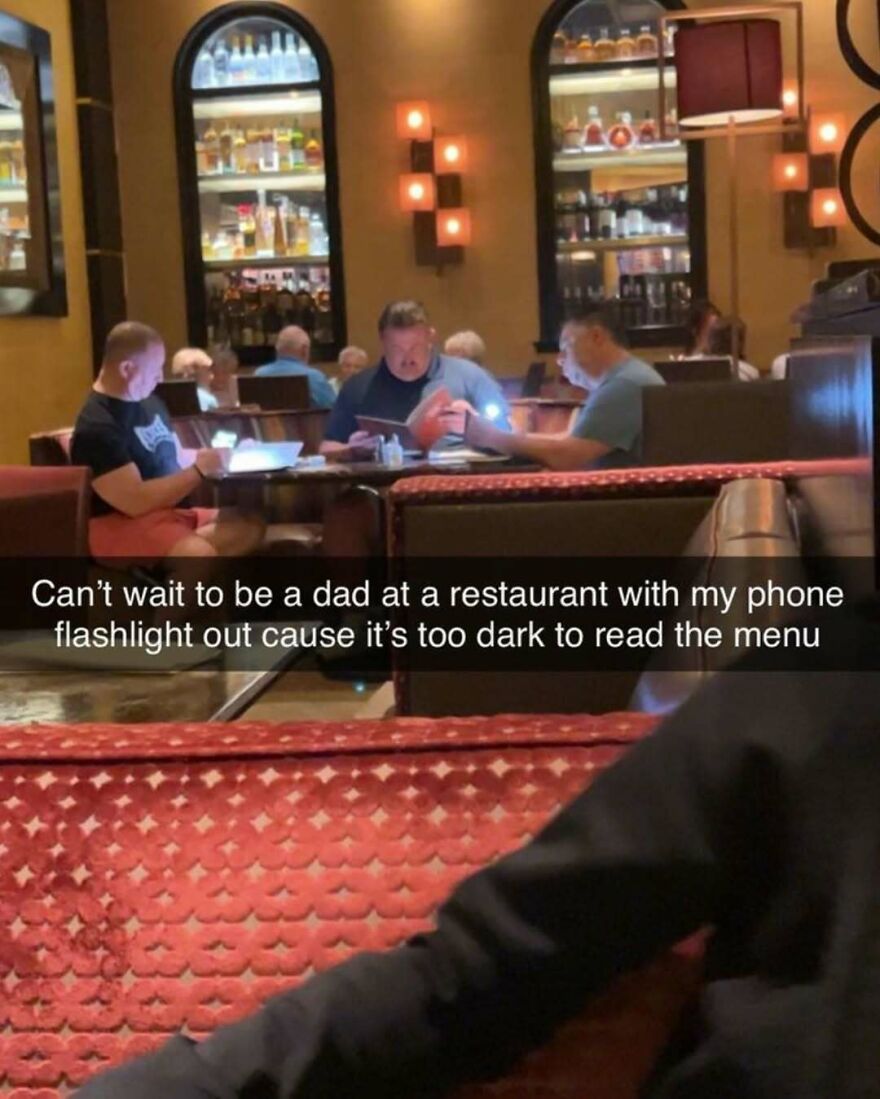 Group of dads using phone flashlight to read menu in dim restaurant, showcasing classic dad behavior in a casual dining setting