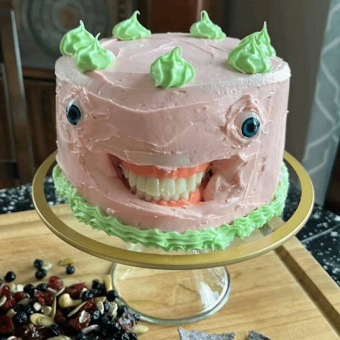 Pink and green cake with realistic fake teeth and eyes, a creepy image that might need a priest or an exorcist.